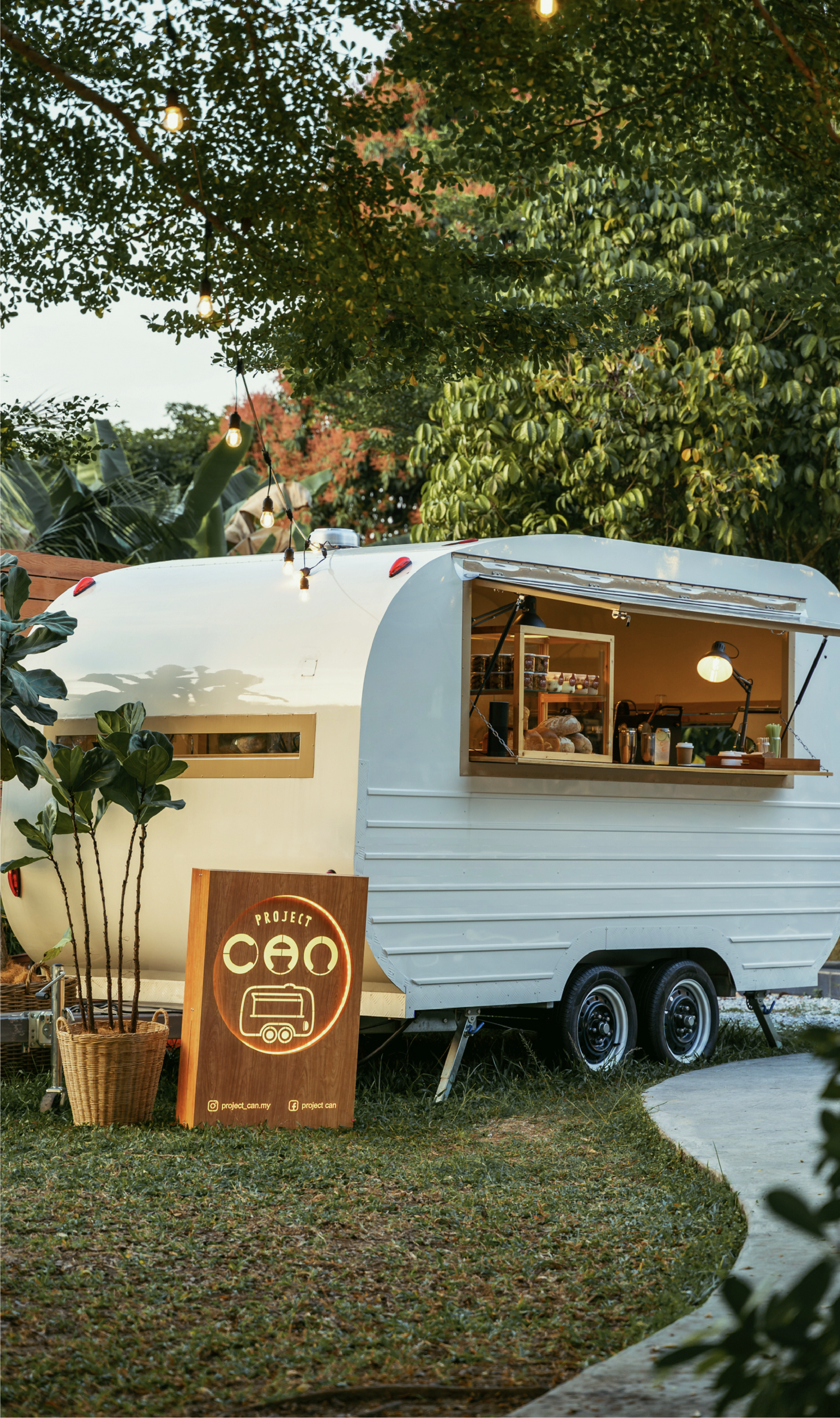 Project CAN caravan café surrounded by trees and lanterns at golden hour.
